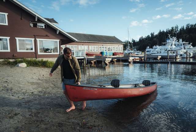Instagram influence @JasonCharlesHill takes a red kayak out of water during their trip to Bellevue. The water is clear, the sky is blue and there are large yachts and evergreens in the background